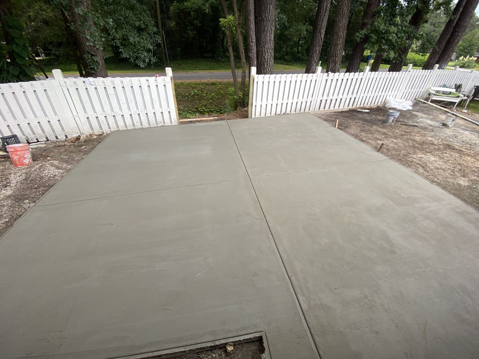 A concrete driveway is being built in front of a white picket fence.