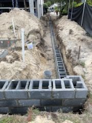 A brick wall is being built next to a trench in the dirt.