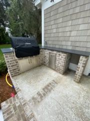A grill is sitting on top of a brick patio next to a brick wall.