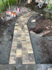 A brick walkway is being built in a backyard.