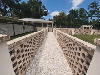 A brick walkway leading to a house with trees in the background