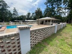 A brick fence surrounds a swimming pool and a house.