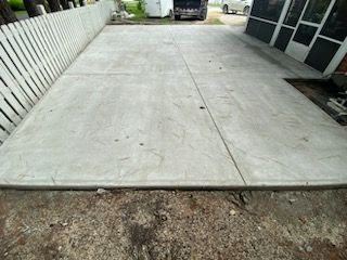 A concrete driveway with a white fence and a car parked in it.