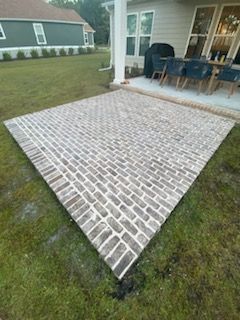 A brick patio with a table and chairs on it in front of a house.
