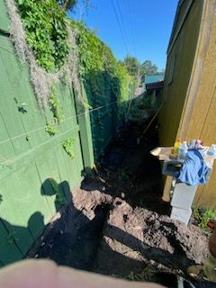 A person is digging in the dirt next to a green fence.
