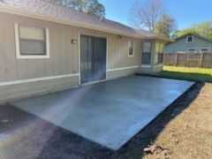 A concrete patio in front of a house with a sliding glass door.