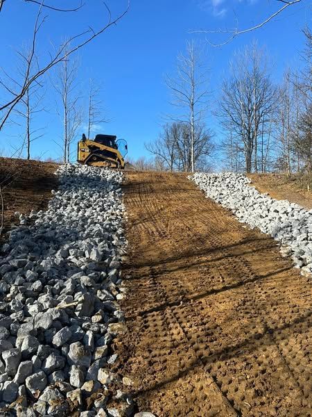 A bulldozer is driving down a dirt road next to a pile of rocks.
