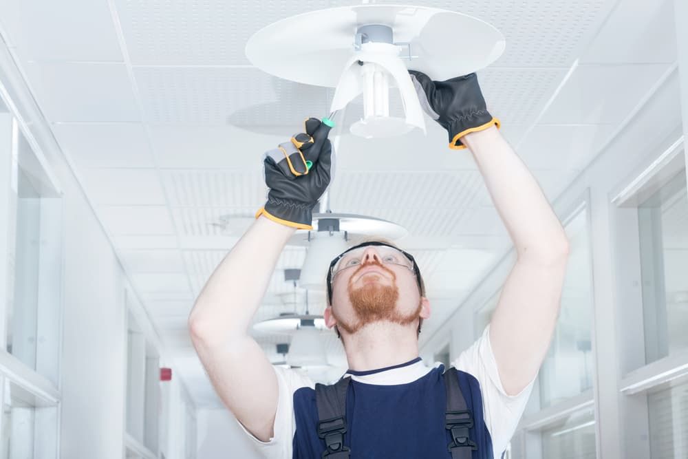 A Man Is Fixing a Light Fixture in A Hallway — Hantis Electrical Solutions in Sanctuary Point, NSW