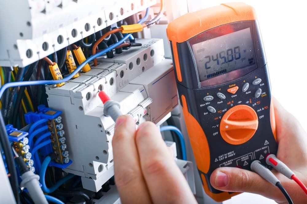 A Person Is Holding a Multimeter in Front of An Electrical Box — Hantis Electrical Solutions in North Nowra, NSW