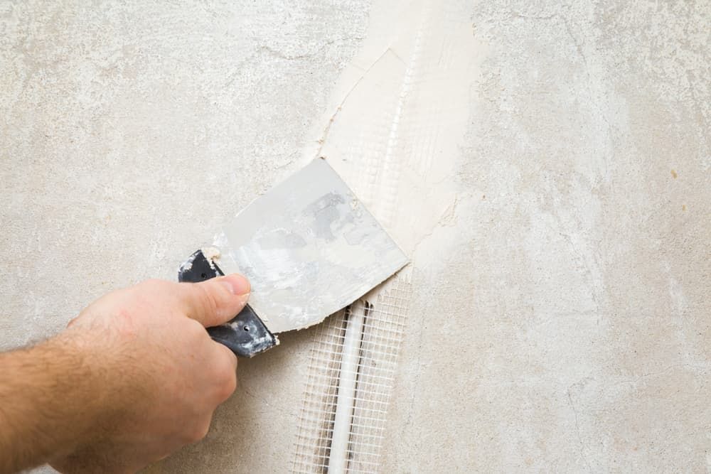 A Person Is Plastering a Wall with A Spatula — Hantis Electrical Solutions in North Nowra, NSW