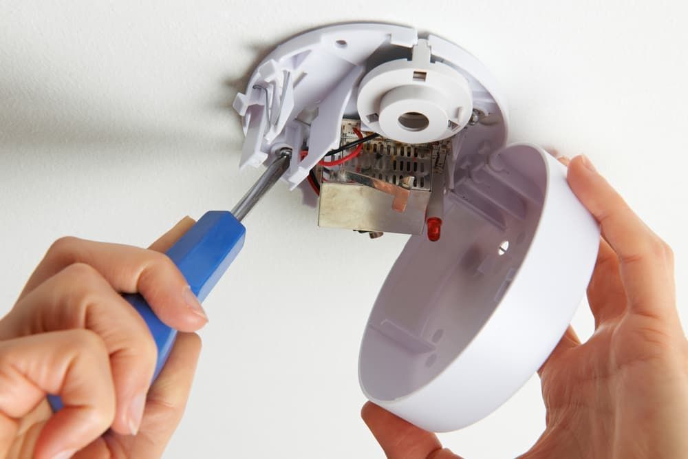 A Person Is Fixing a Smoke Detector with A Screwdriver — Hantis Electrical Solutions in North Nowra, NSW