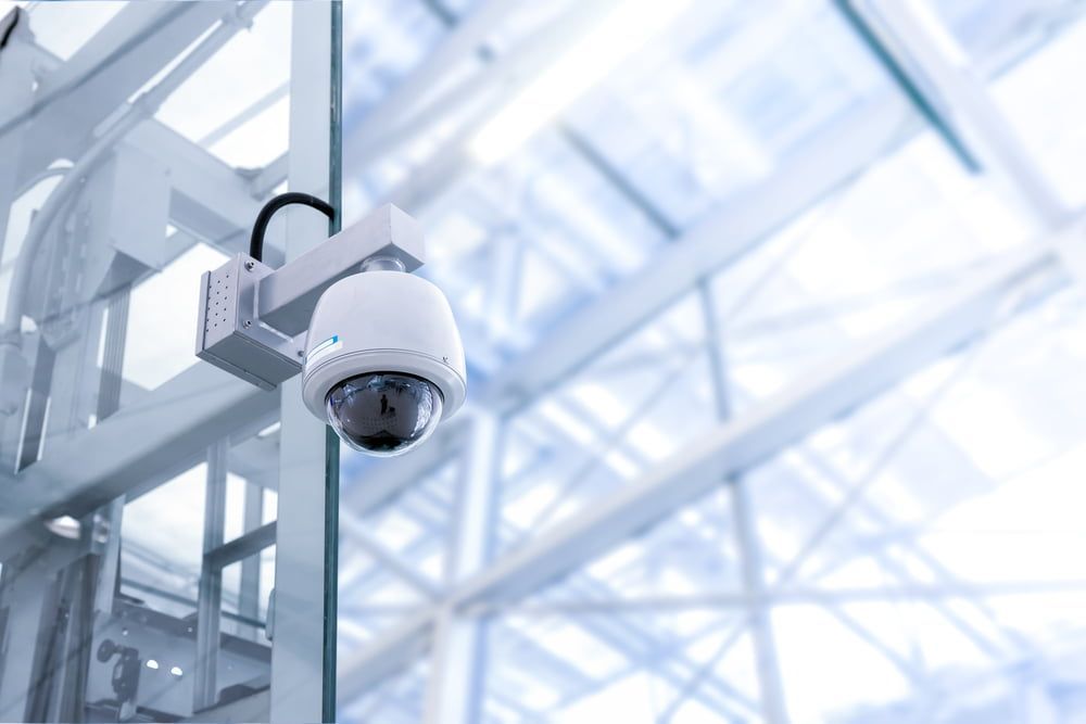 A Security Camera Is Hanging from A Glass Wall in A Building — Hantis Electrical Solutions in North Nowra, NSW