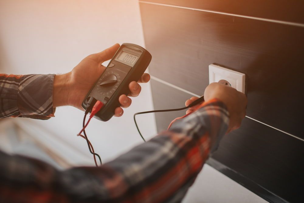 A Man Is Using a Multimeter to Test an Electrical Outlet — Hantis Electrical Solutions in North Nowra, NSW