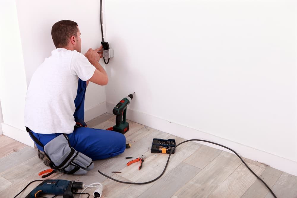 A Man Is Sitting on The Floor Working on A Wall — Hantis Electrical Solutions in Sanctuary Point, NSW