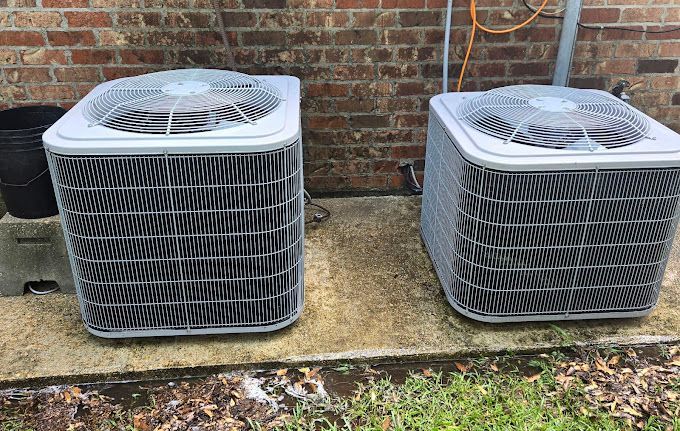 Two air conditioners are sitting next to each other on the side of a brick building.
