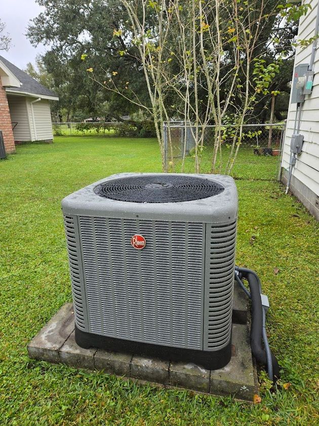 A gray air conditioner is sitting on top of a concrete block in a backyard.