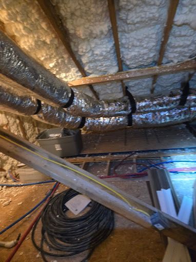 A ladder is sitting in the attic next to a bunch of pipes.