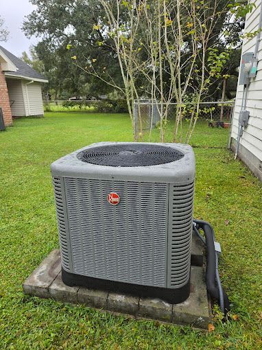An air conditioner is sitting on top of a concrete block in the backyard of a house.
