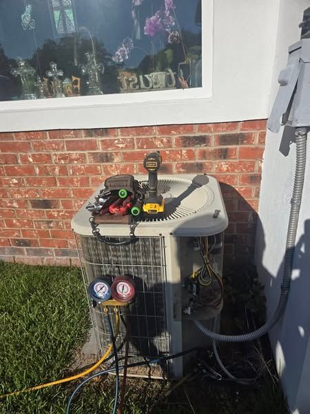 An air conditioner is sitting on the side of a brick building next to a window.