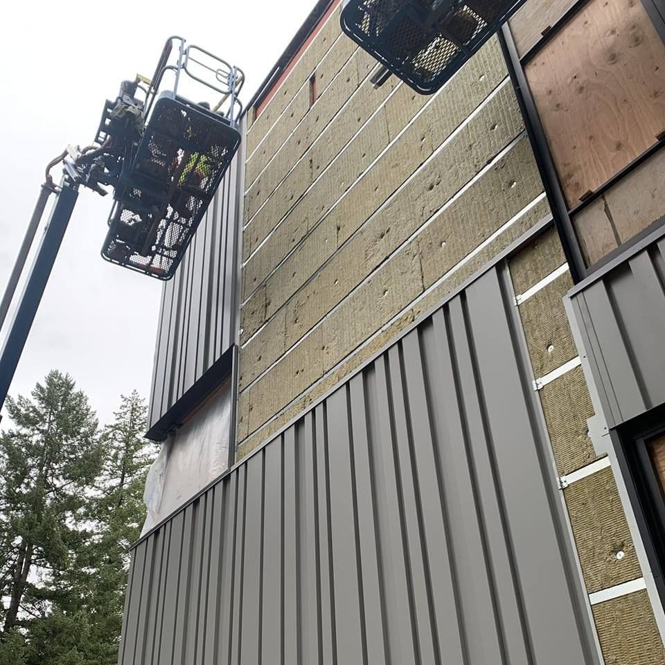 Construction workers in lift installing metal siding on a building with exposed insulation. Gray tones.