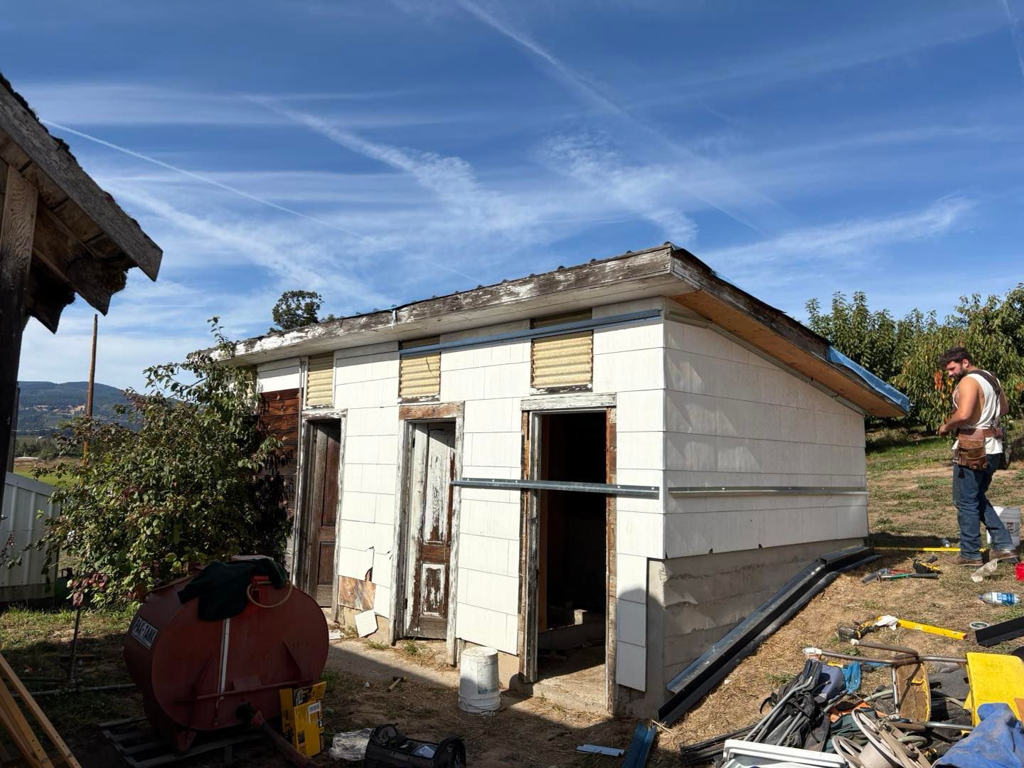 Small white building under construction; man working nearby on a sunny day.