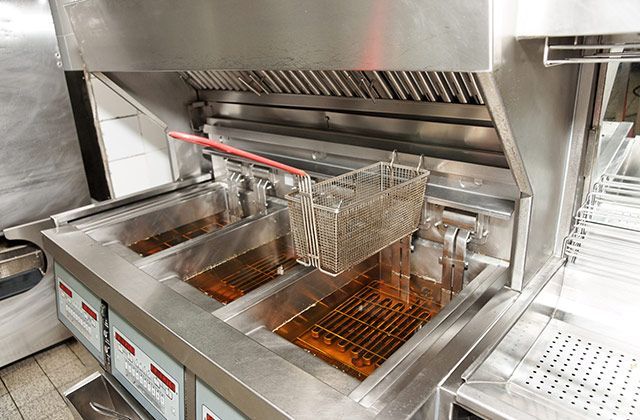A stainless steel fryer is filled with oil in a kitchen.