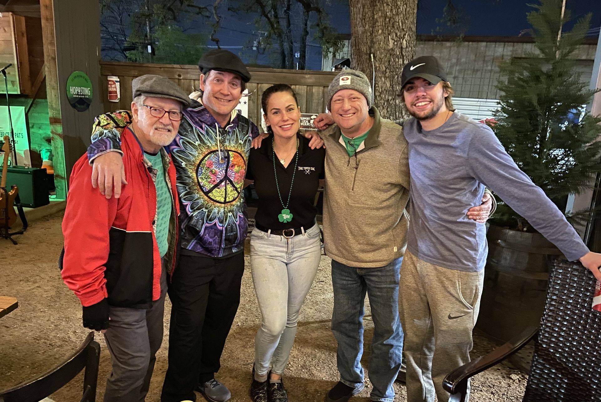 Five people smiling and posing for a photo outside a venue. The group has their arms around each other.