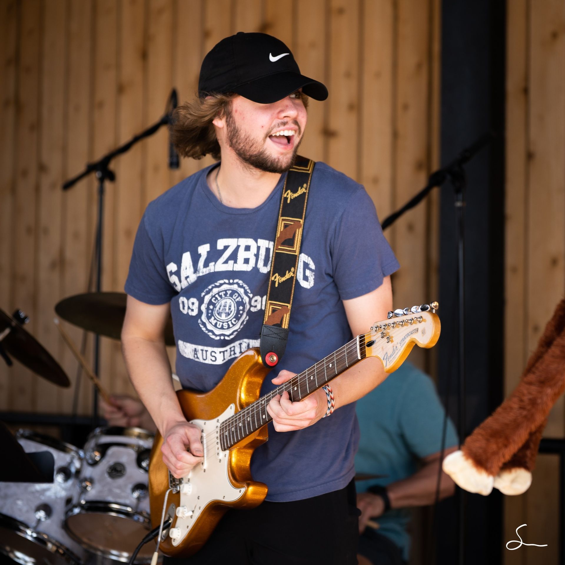 A young man plays a golden guitar, wearing a baseball cap and a blue 
