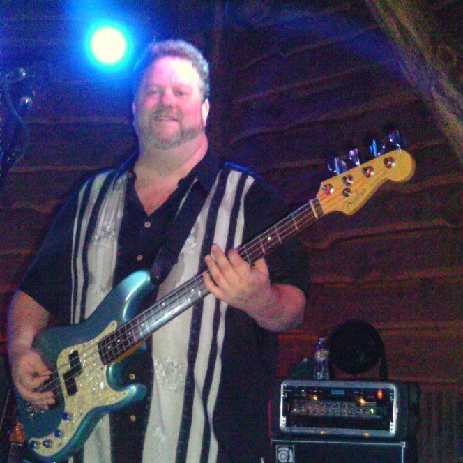 Man playing a blue bass guitar on stage, wearing a striped shirt.