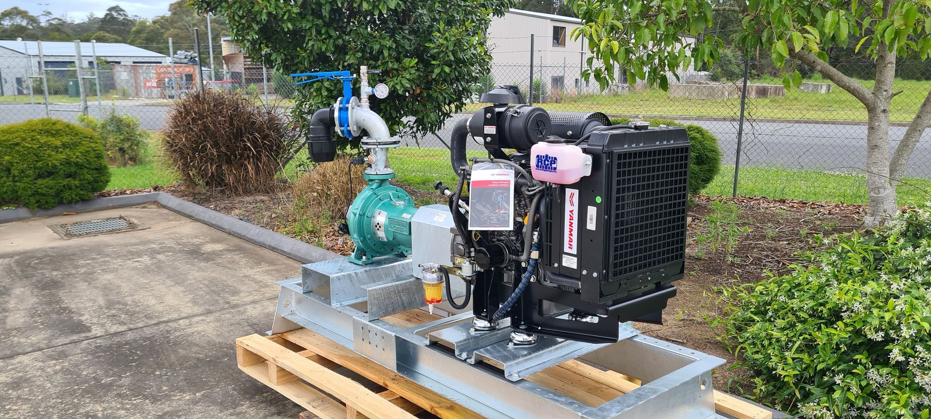 A Water Pump Is Sitting Next To A Black Tank In A Field — Midcoast Irrigation & Horticultural Supplies In Wauchope, NSW