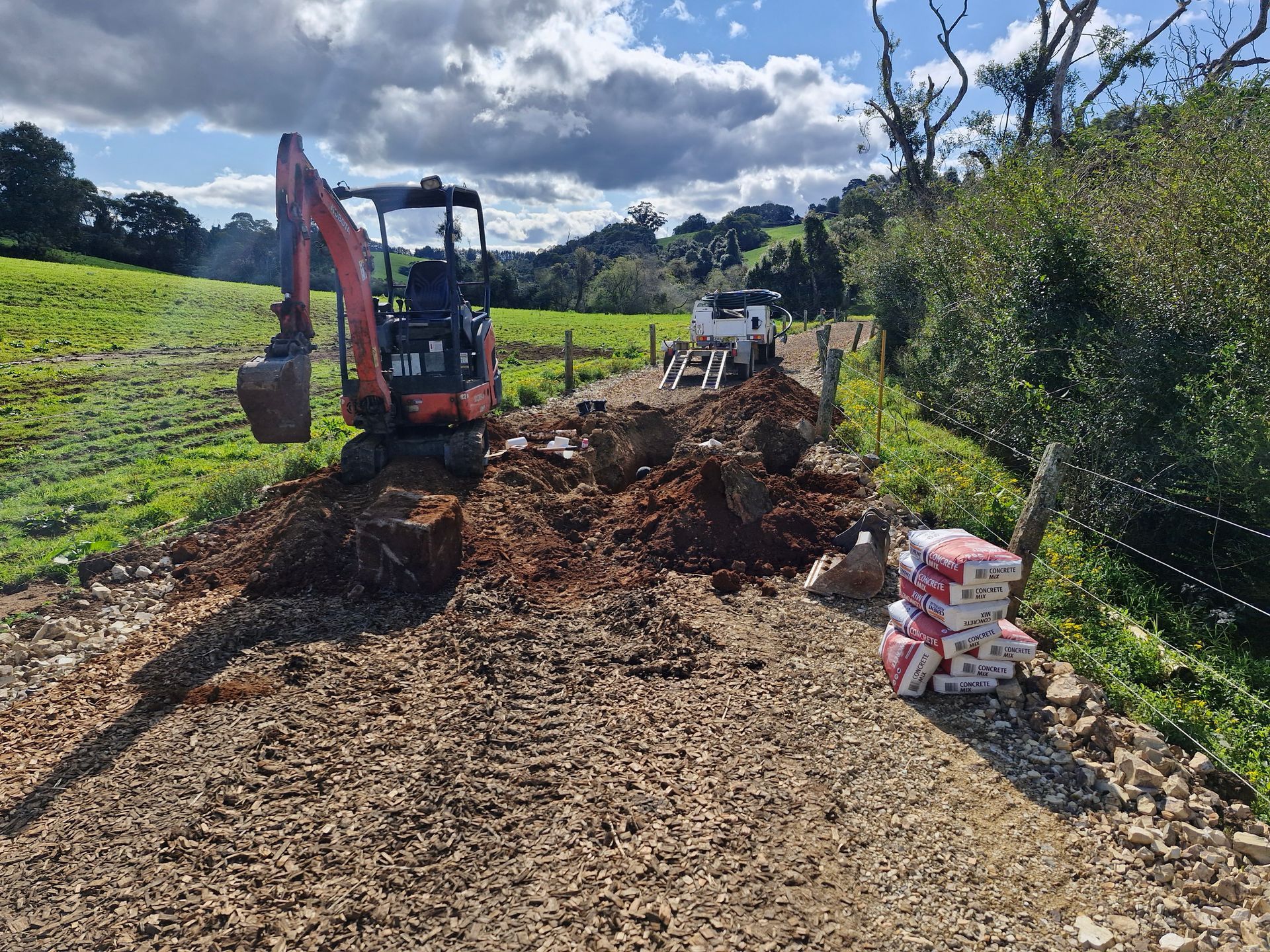 An excavator is digging a hole in the dirt on a dirt road.— Midcoast Irrigation & Horticultural Supplies In Wauchope, NSW