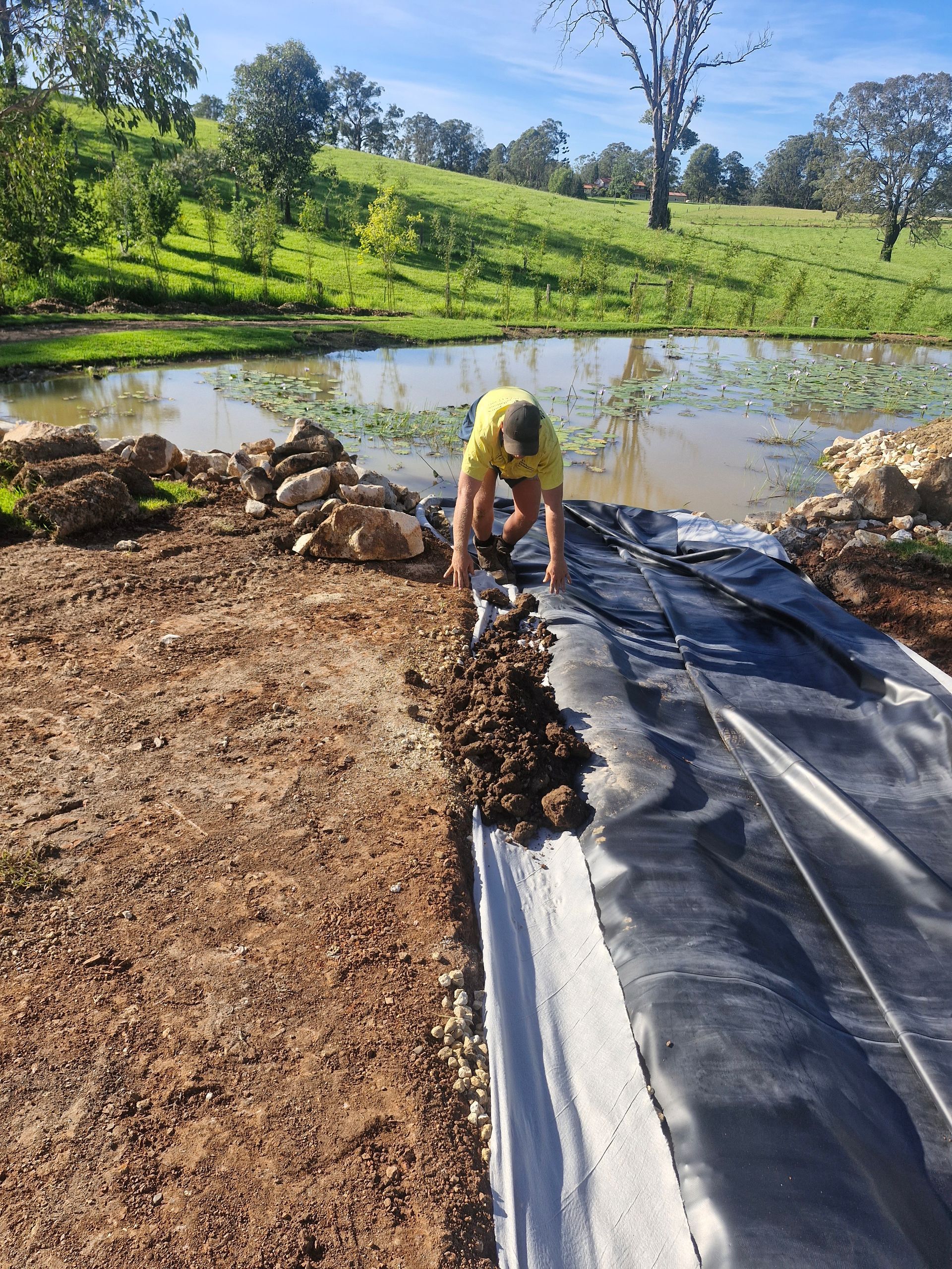 A man is laying a tarp over a body of water.— Midcoast Irrigation & Horticultural Supplies In Laurieton, NSW