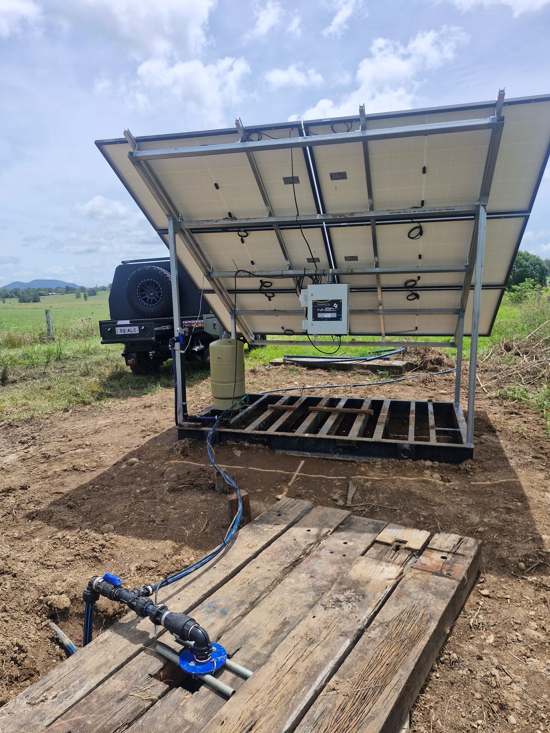 A solar panel is sitting on top of a wooden platform in a field.— Midcoast Irrigation & Horticultural Supplies In Sancrox, NSW
