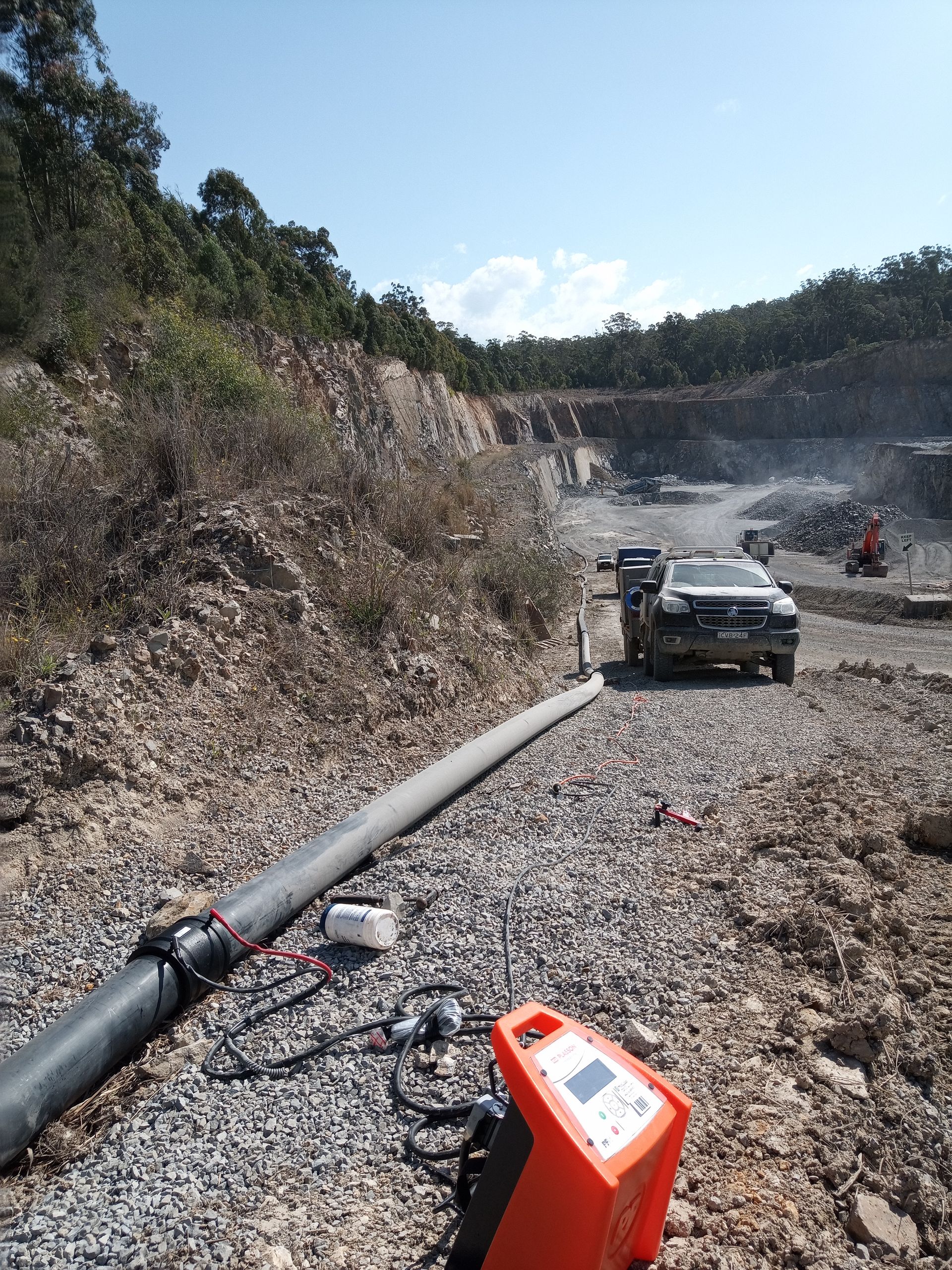 A Large Hose Is Running Down A Construction Site With A Truck Parked In The Background And A Machine Measuring The Hose — Midcoast Irrigation & Horticultural Supplies In Wauchope, NSW