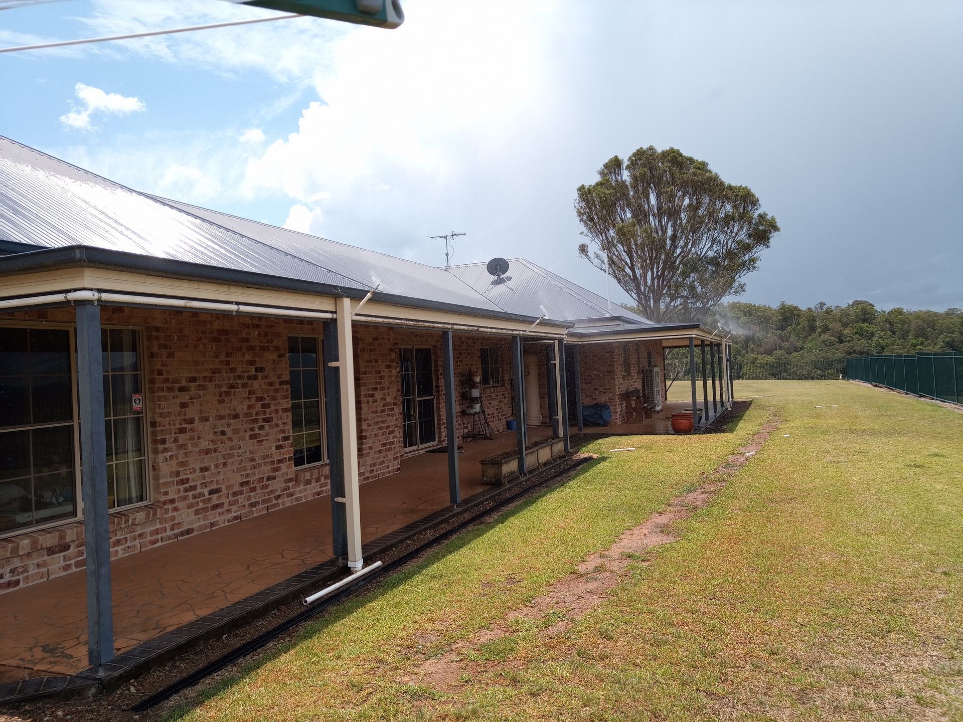 A House With Irrigation Systems Spraying Over The Gutter Line With A Tree  In The Background And A Large Bit Of Lawn On The Right — Midcoast Irrigation & Horticultural Supplies In Wauchope, NSW