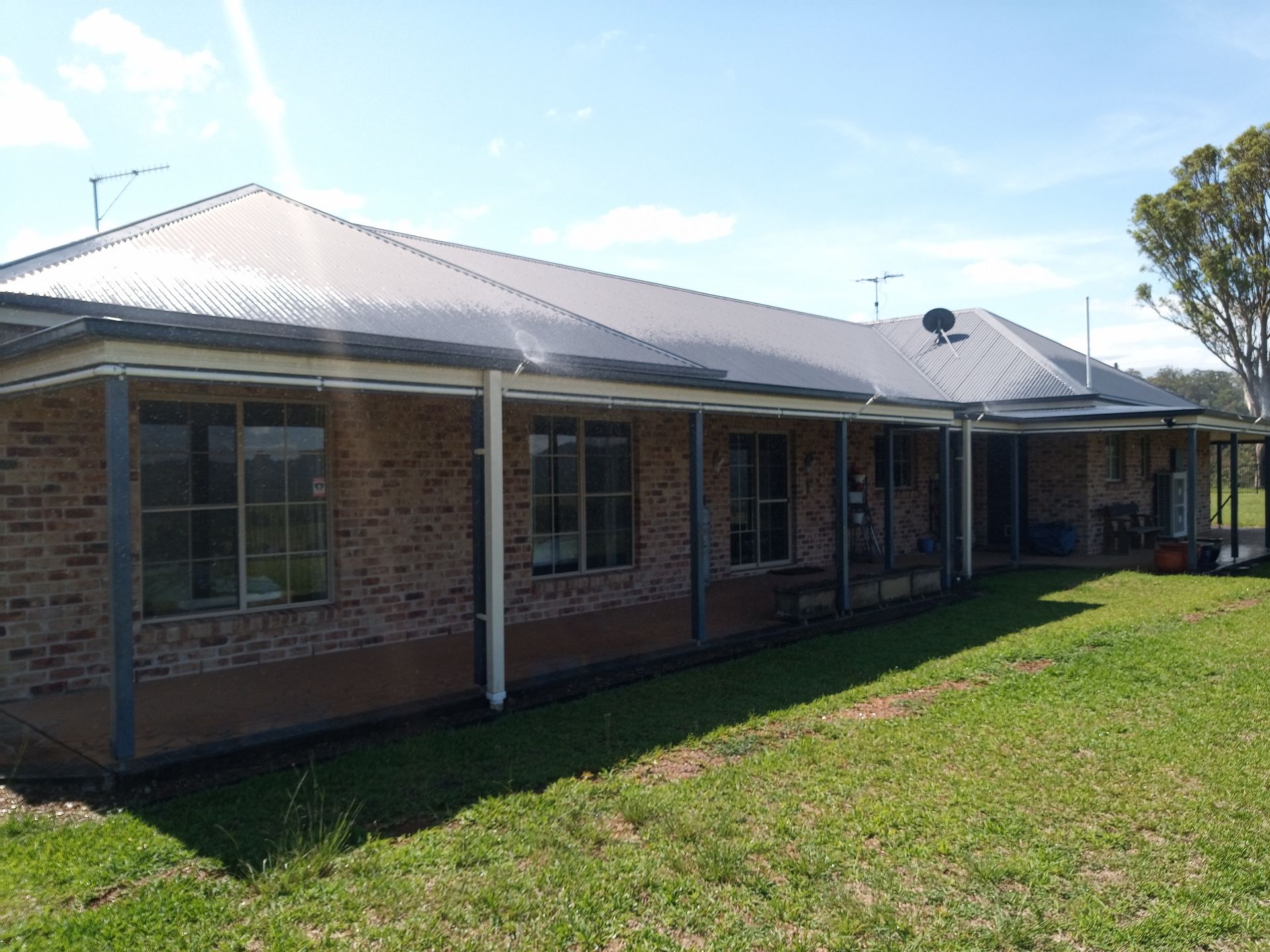 A large brick house with a metal roof is sitting on top of a lush green field.— Midcoast Irrigation & Horticultural Supplies In Wauchope, NSW