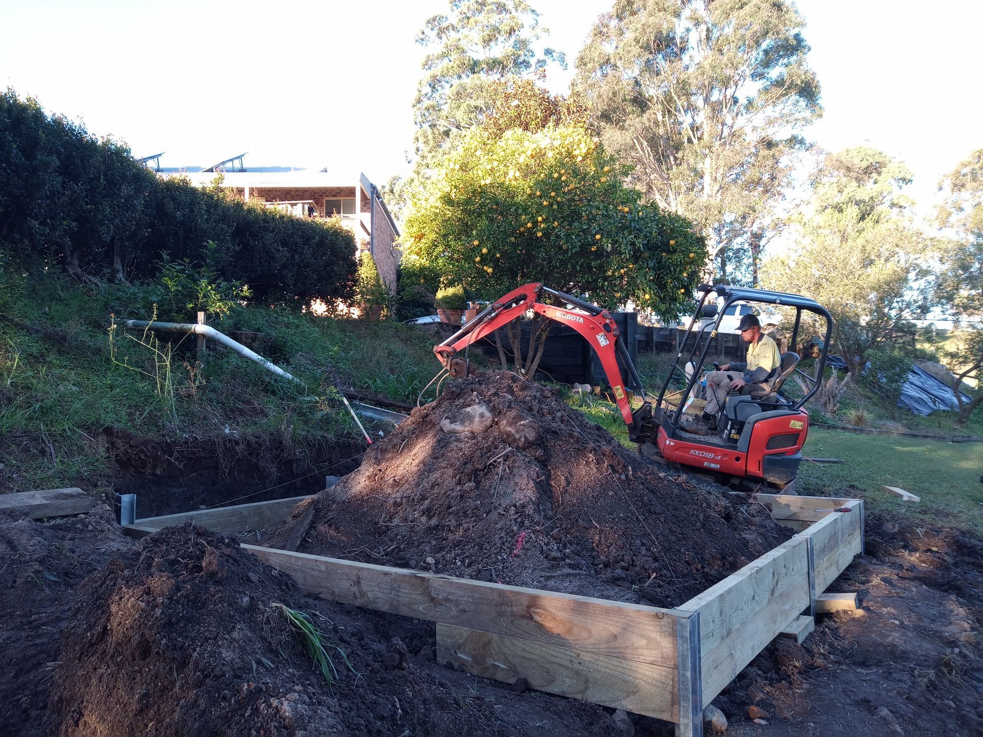 A small red excavator is digging a hole in the ground.— Midcoast Irrigation & Horticultural Supplies In Wauchope, NSW