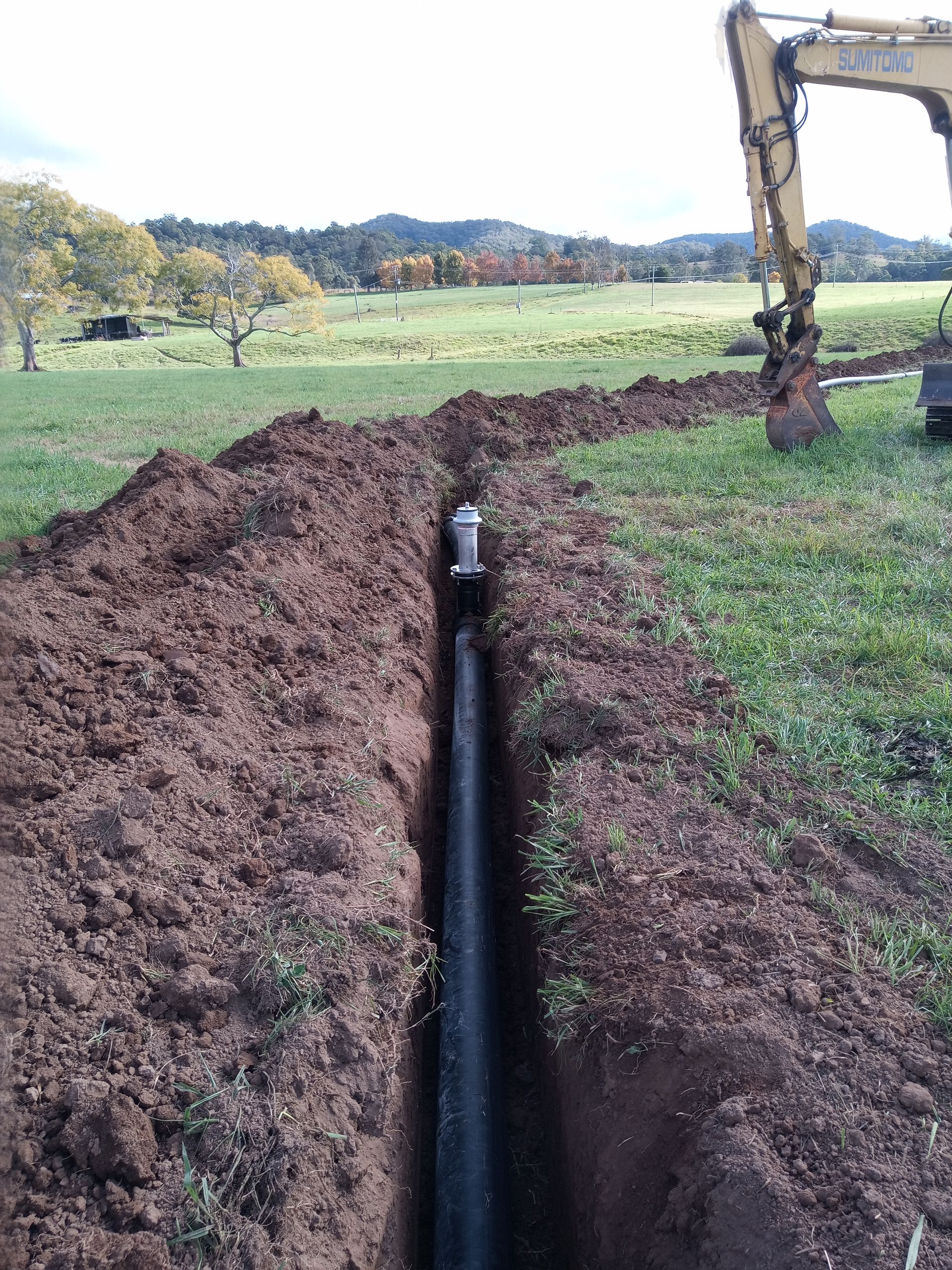 A pipe is being installed in a trench in a field.— Midcoast Irrigation & Horticultural Supplies In Wauchope, NSW