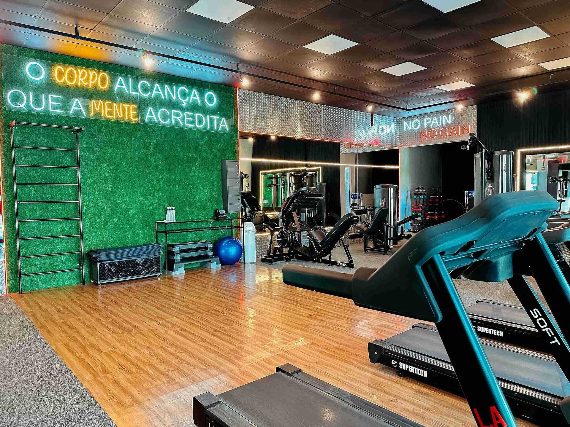 Espaço fitness moderno do Enotel Porto de Galinhas com esteiras ergométricas e parede verde decorada com letreiro neon motivacional.