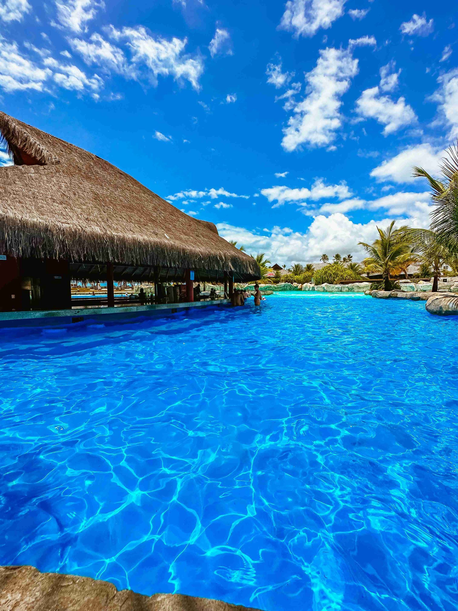 Bar molhado sob grande quiosque de palha na piscina azul do resort all inclusive Enotel Porto de Galinhas