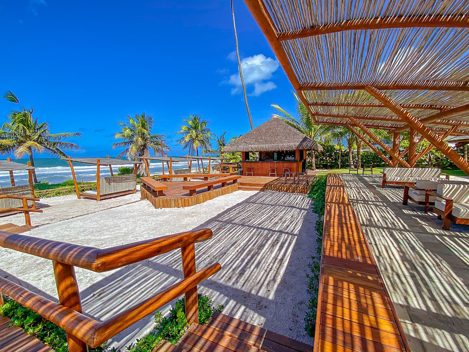 Deck de madeira à beira-mar com estrutura de bambu para sombra e bar rústico. Vista para a praia e o mar de Porto de Galinhas, Pernambuco.