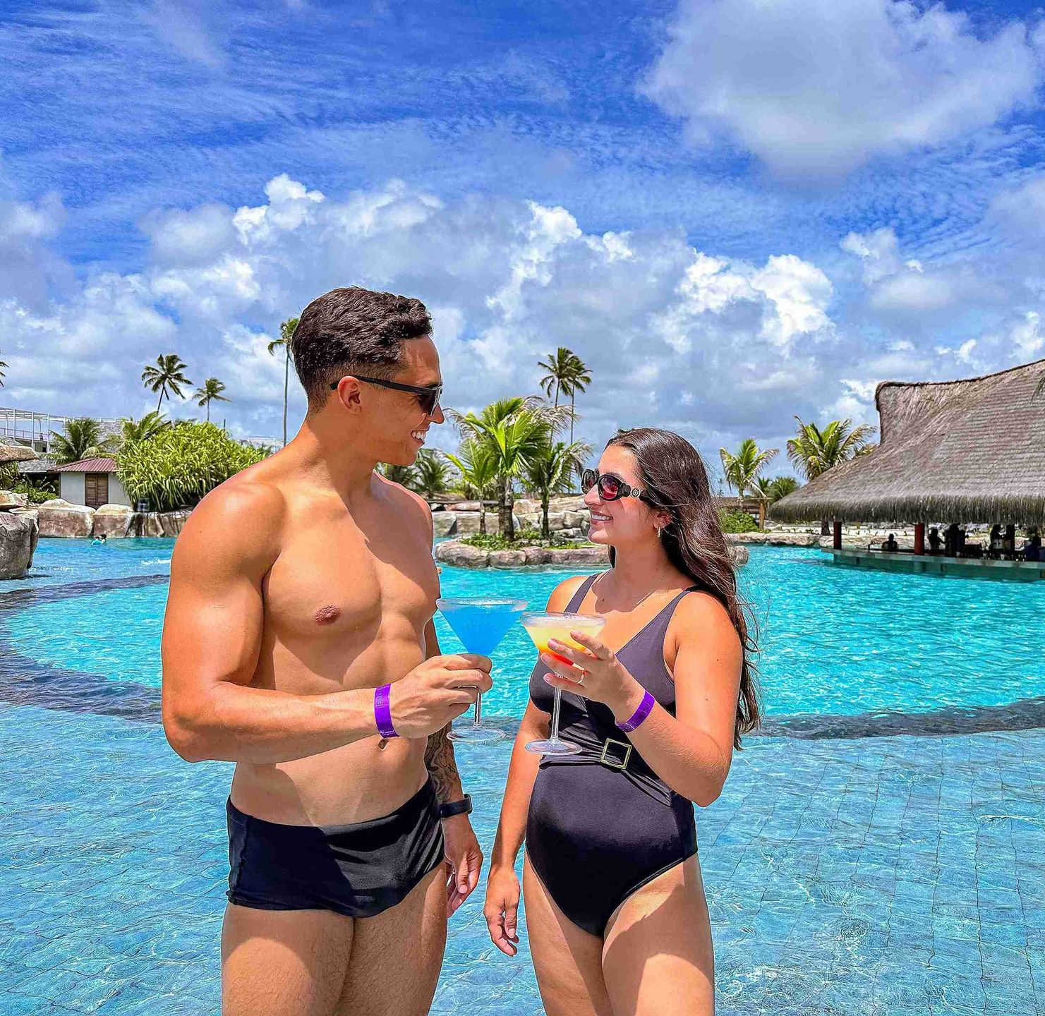 Casal brindando com coquetéis coloridos à beira da piscina do Enotel Porto de Galinhas, aproveitando as experiências do sistema all inclusive