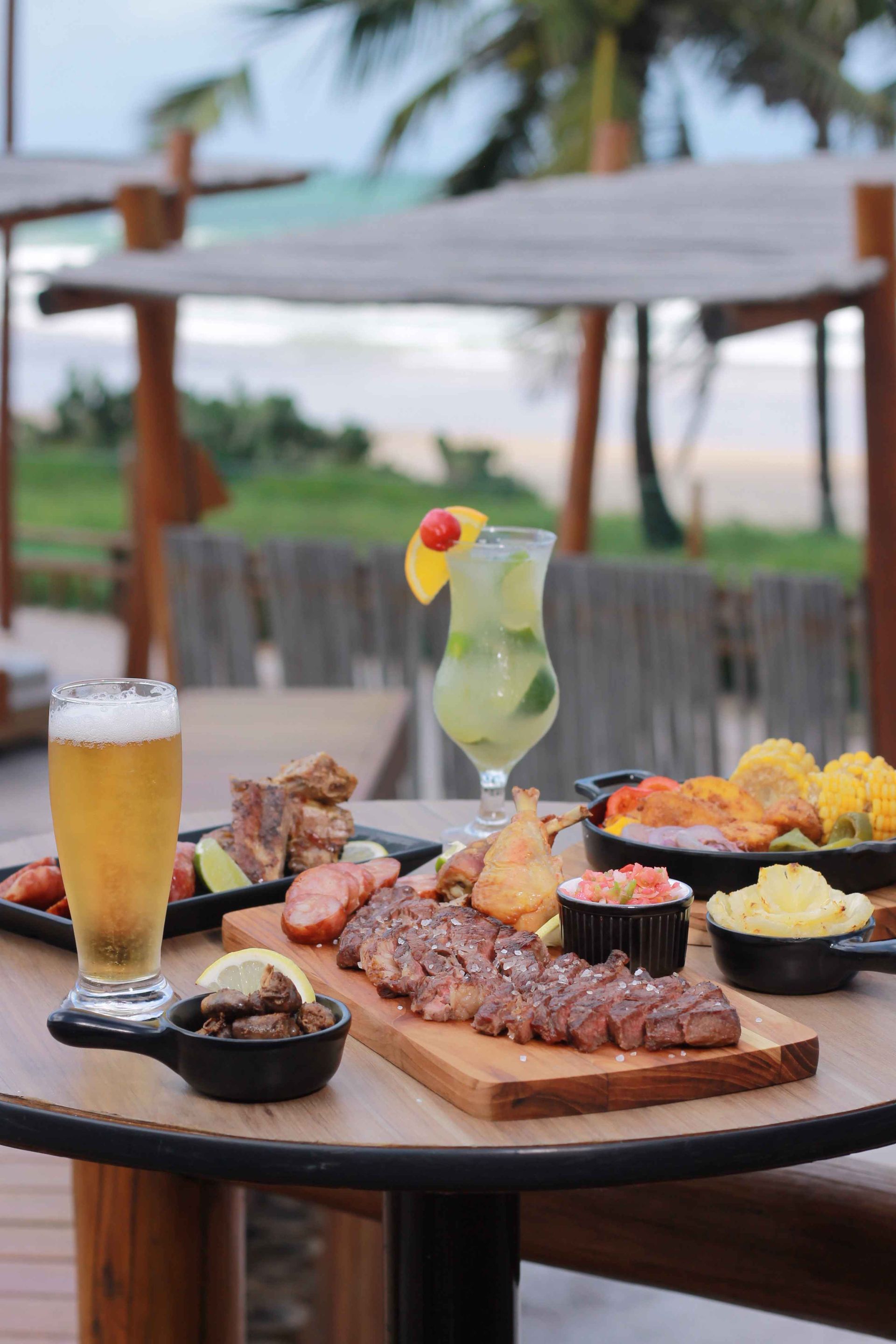 Tábua de carnes grelhadas, chopp gelado e drink tropical à beira-mar, destacando a experiência da gastronomia all inclusive do Enotel Porto de Galinhas.