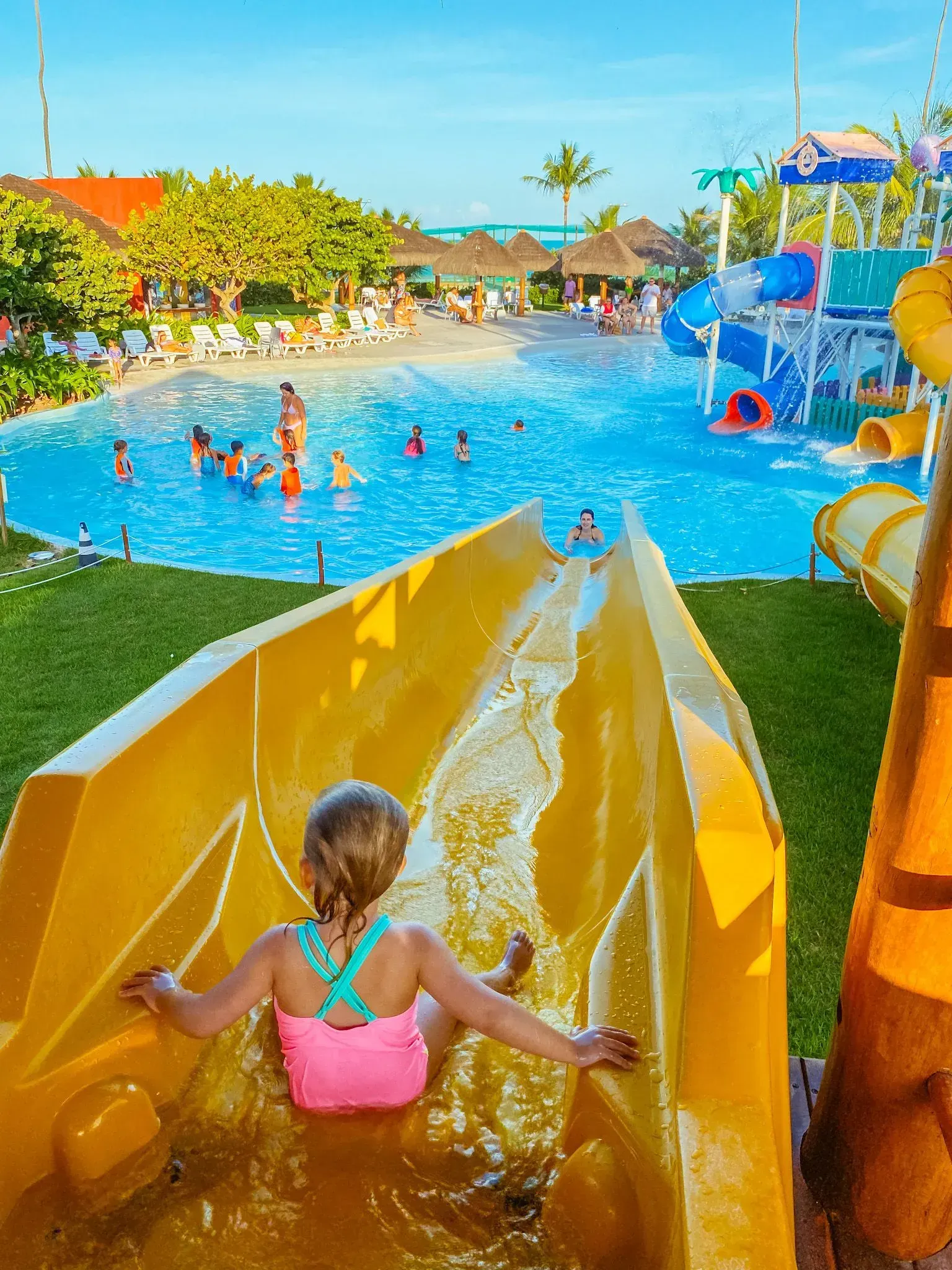 Menina de maiô rosa prestes a descer em um tobogã amarelo no parque aquático infantil do resort Enotel Porto de Galinhas
