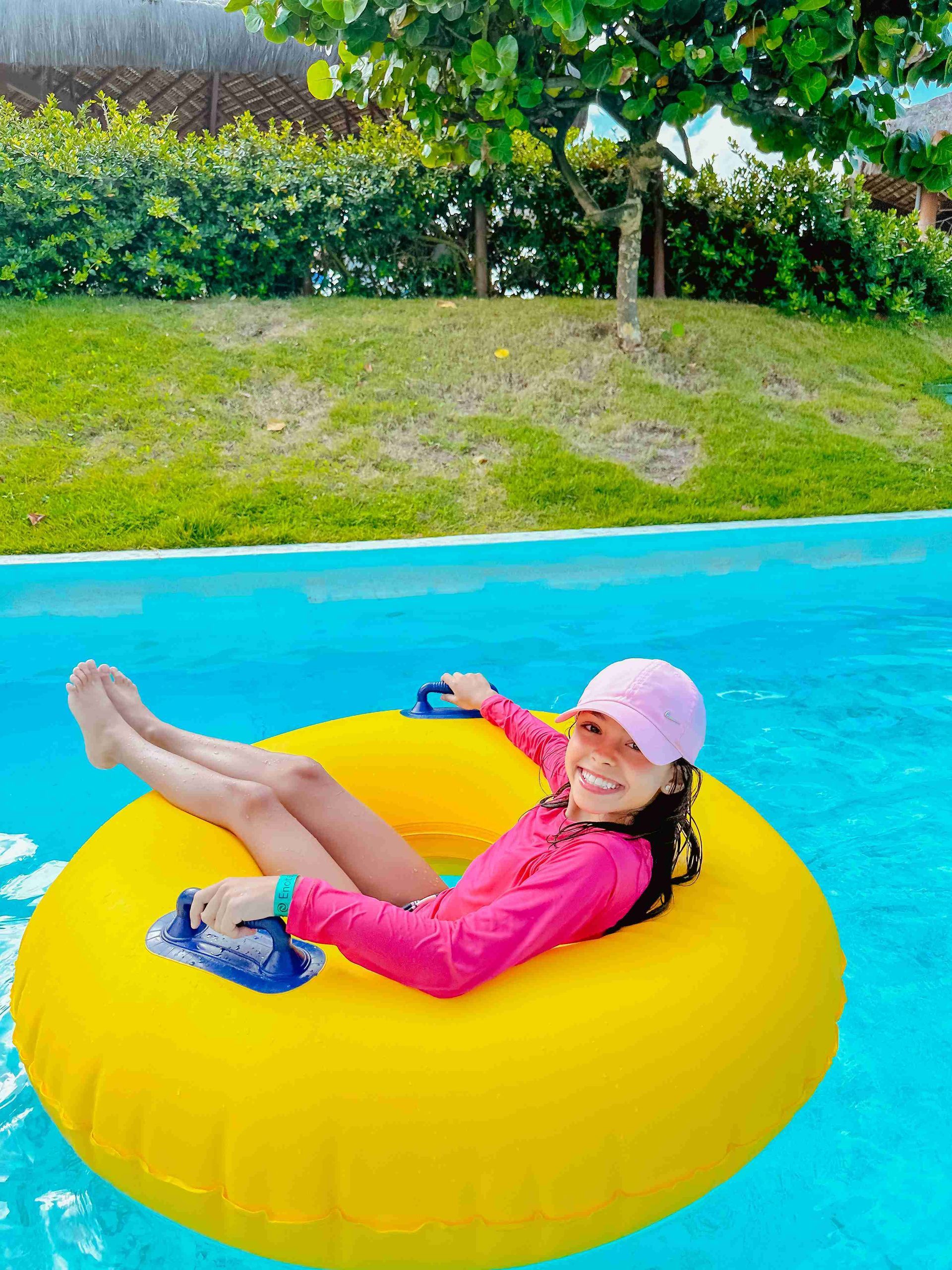 Menina de boné rosa sorrindo em boia amarela no rio lento do parque aquático do resort all inclusive Enotel Porto de Galinhas