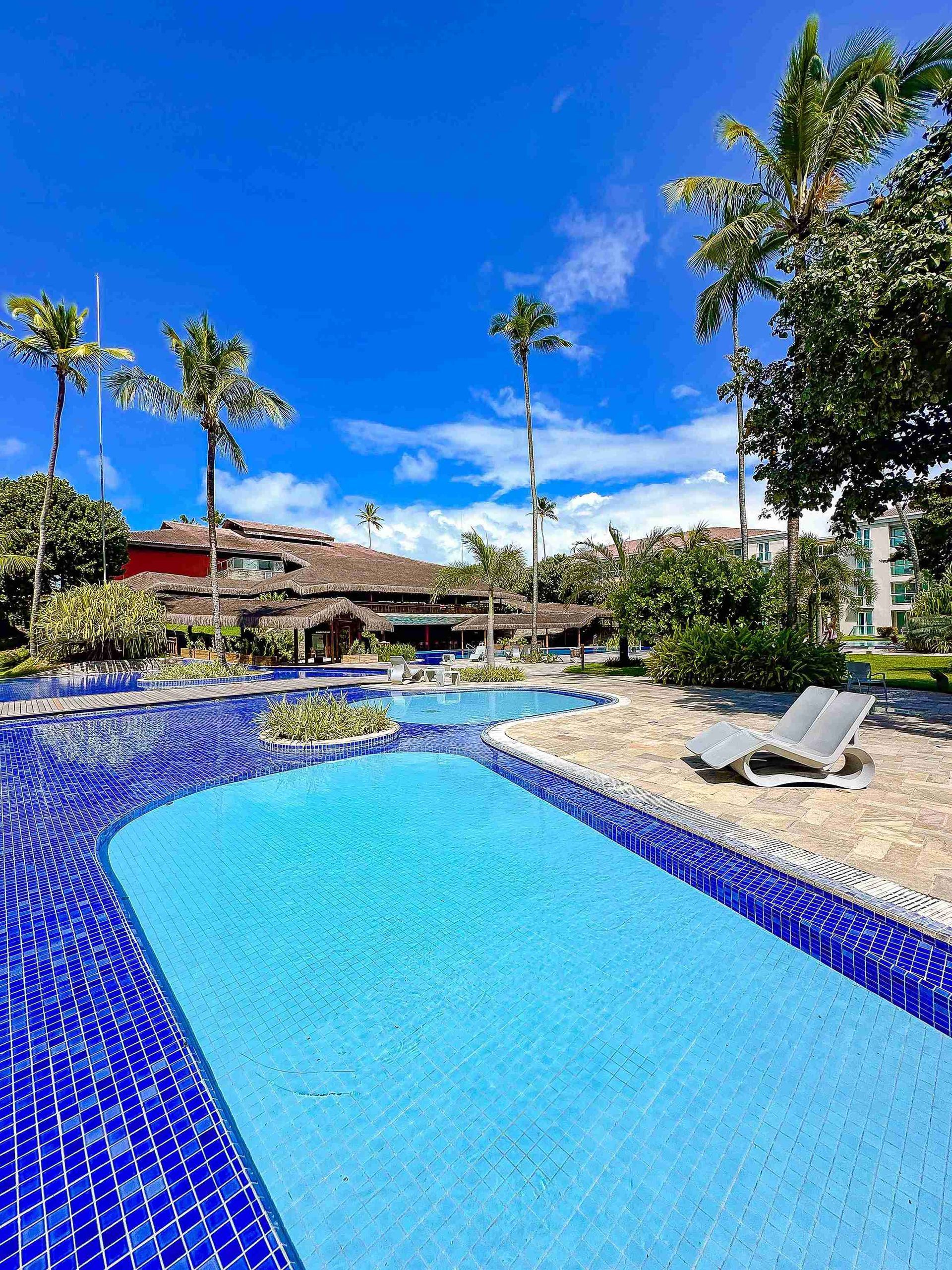 Área de relaxamento com espreguiçadeira à beira de piscinas sinuosas e jardins tropicais no Enotel Porto de Galinhas