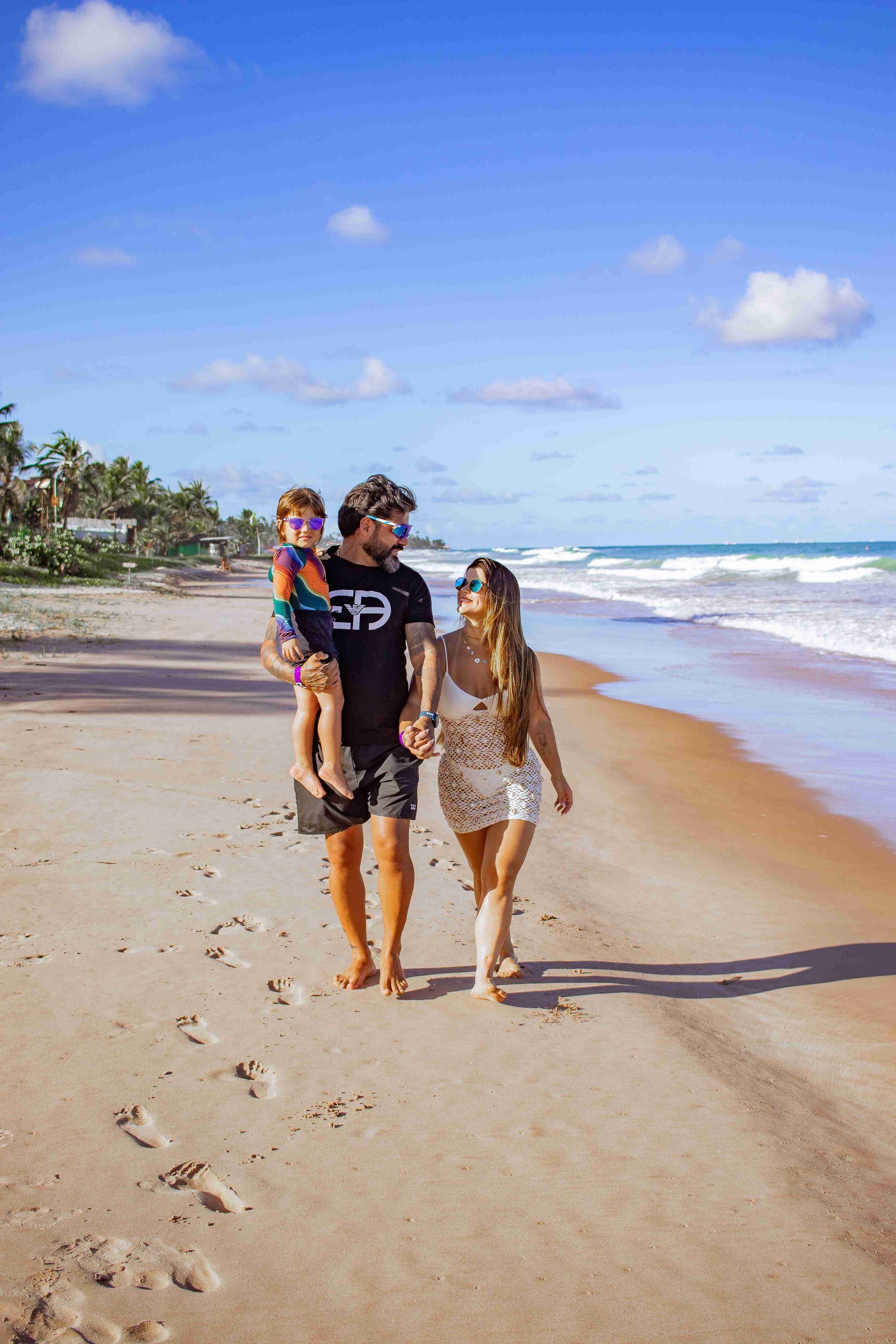 Família caminhando de mãos dadas na areia da praia em frente ao mar, aproveitando o lazer no Enotel Porto de Galinhas