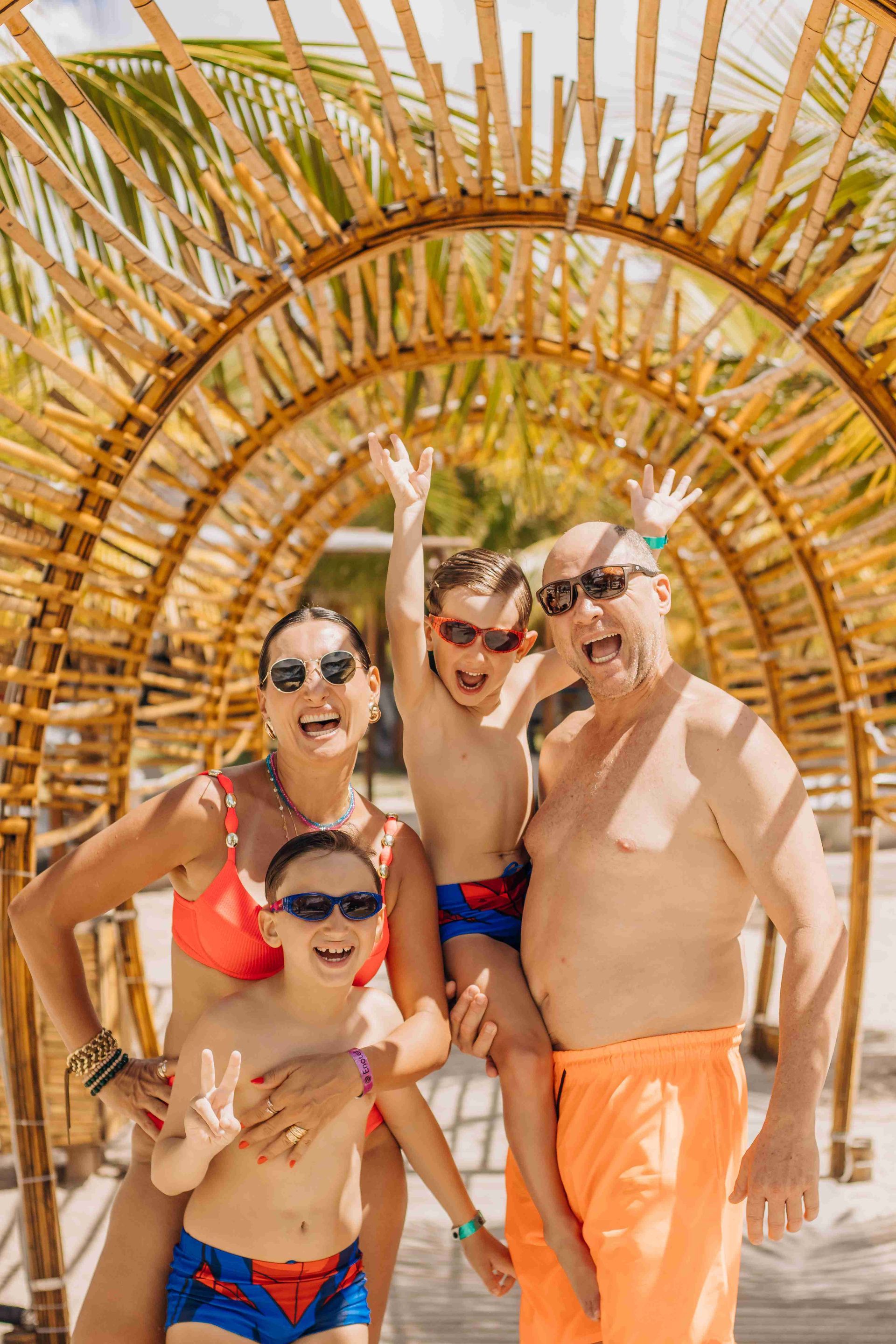 Família feliz com dois filhos sorrindo sob arco de bambu na área de lazer do resort all inclusive Enotel Porto de Galinhas