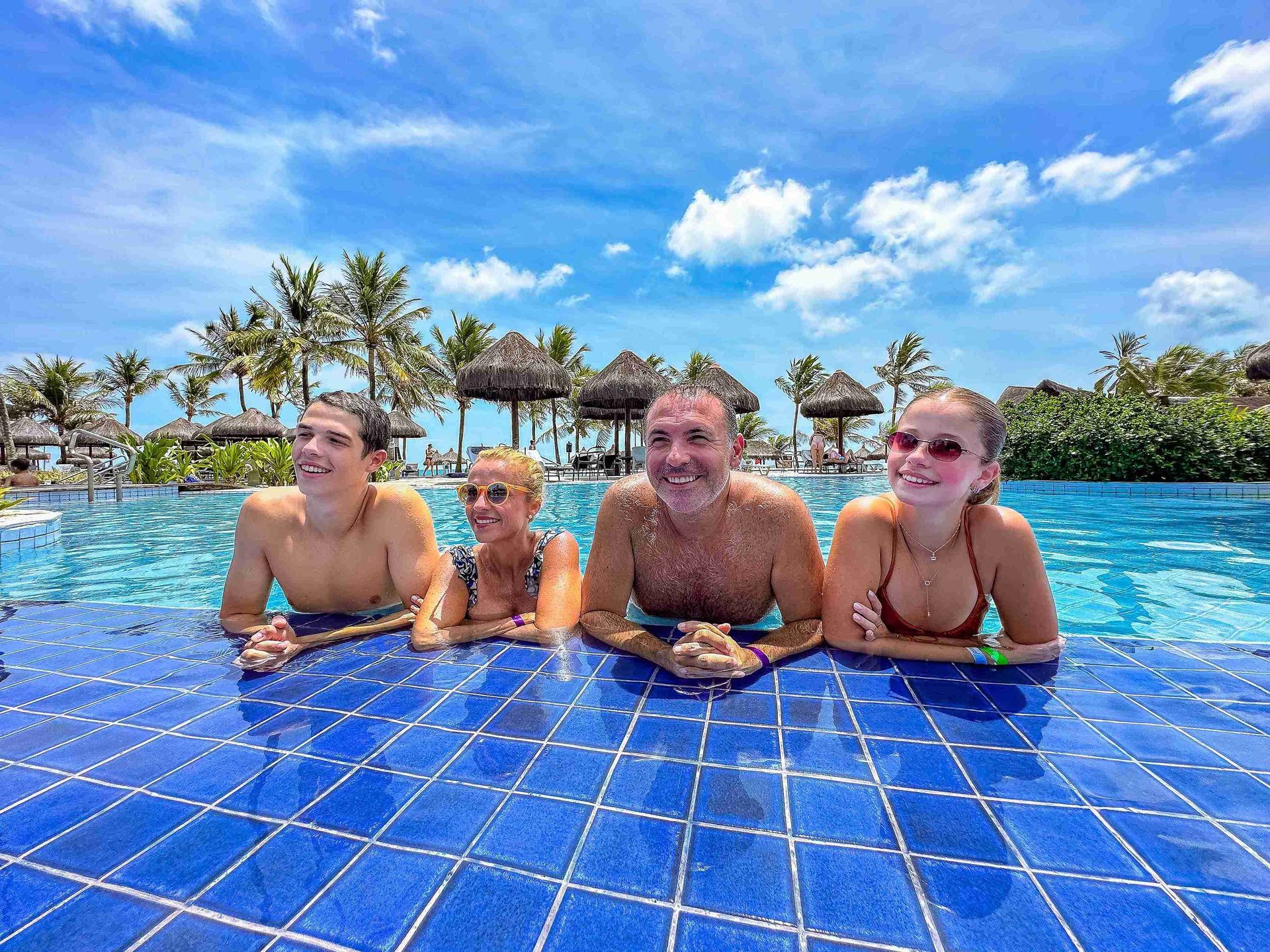 Família reunida na borda de azulejos azuis da piscina principal do Enotel Porto de Galinhas durante férias relaxantes no resort all inclusive