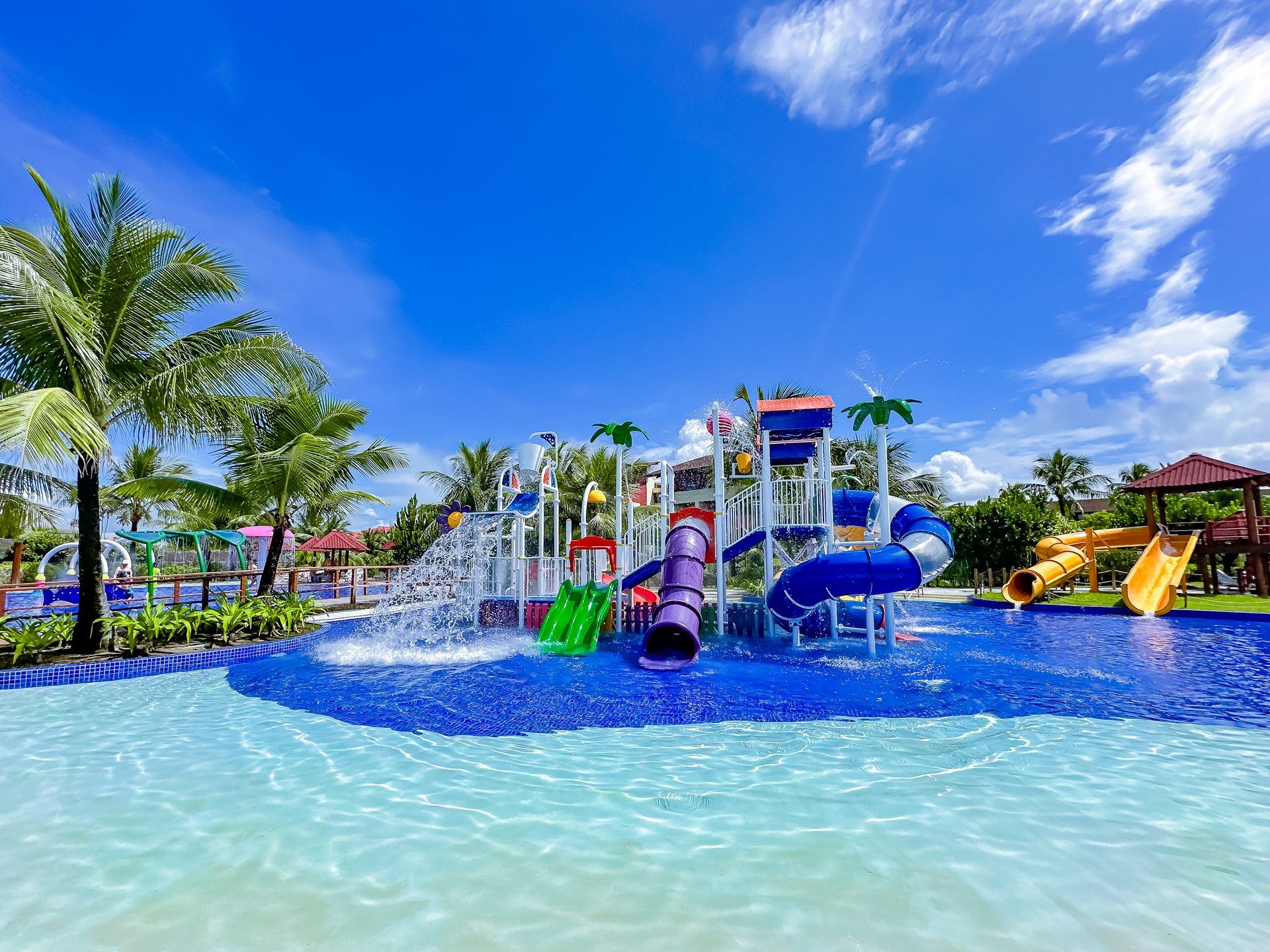 Parque aquático infantil do Enotel Porto de Galinhas com toboáguas coloridos, escorregadores e chafarizes interativos sob céu azul